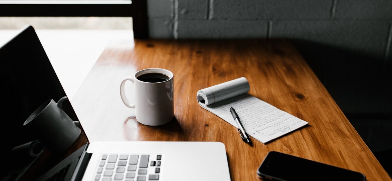 MacBook Pro, white ceramic mug,and black smartphone on table